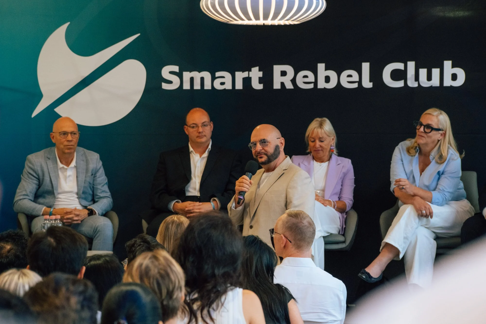 Fünf Personen auf dem Panel vor der Smart-Rebel-Club-Wand, der Mann in der Mitte spricht ins Mikrofon.