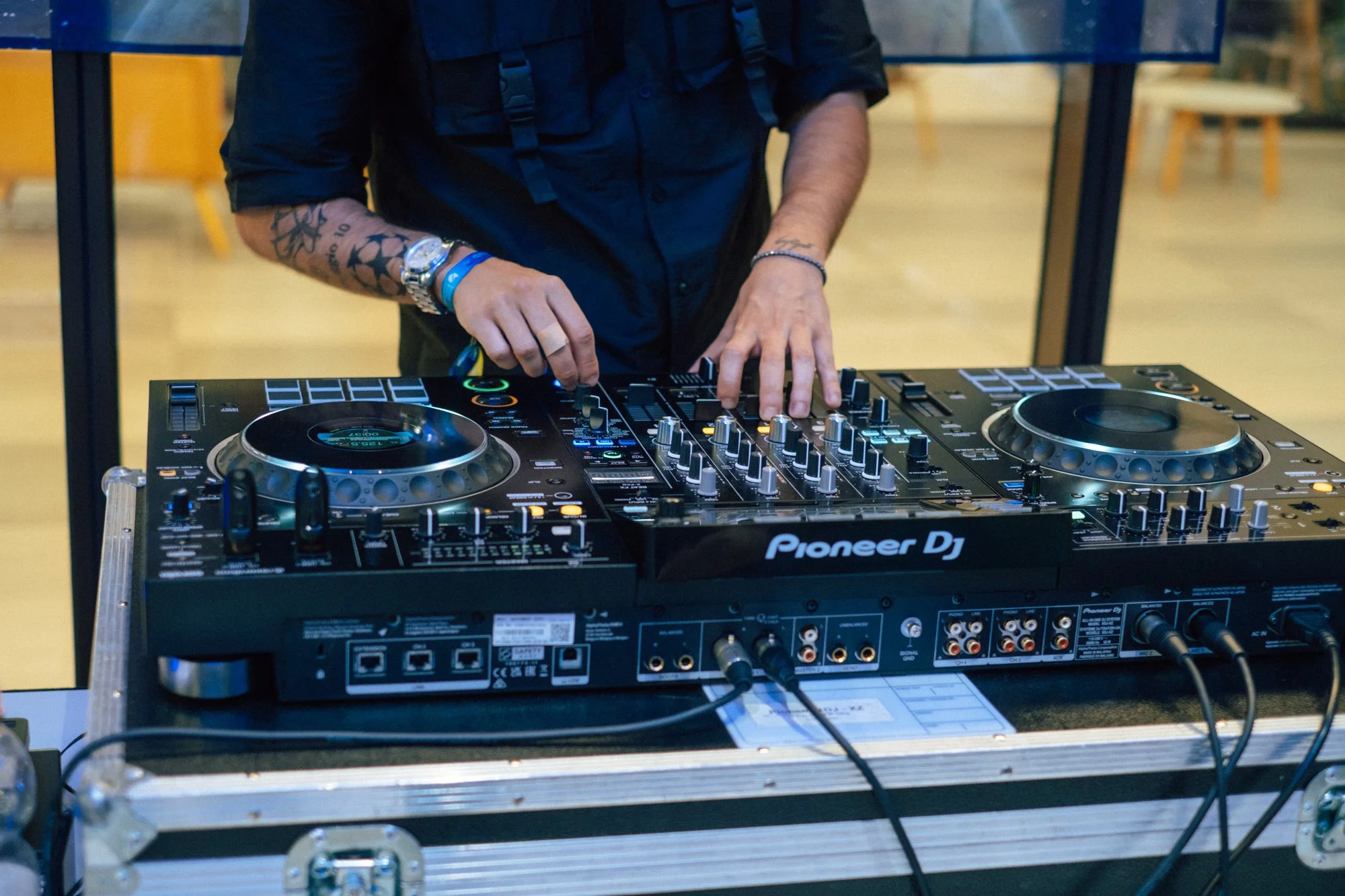 Hände eines DJs an einem Pioneer-Controller, im Hintergrund helles Foyer.