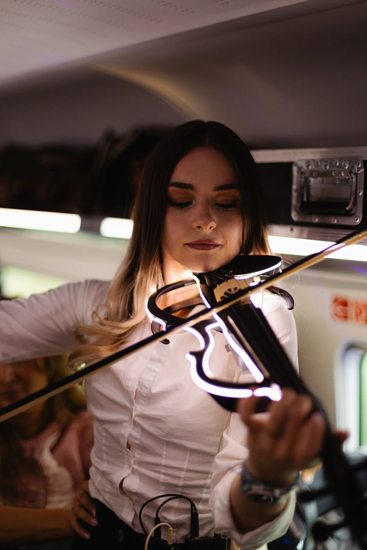 Eine Musikerin spielt im Zug eine weiß leuchtende elektrische Geige.