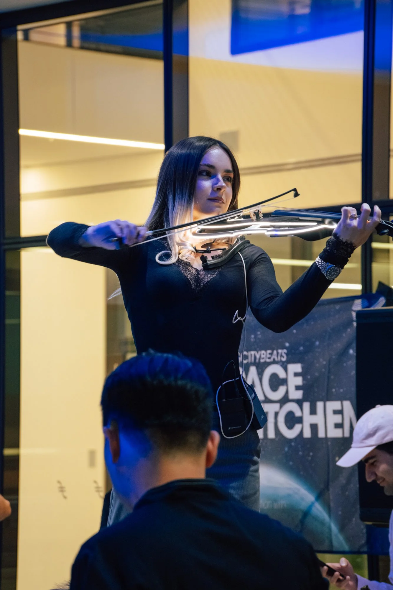 Eine Geigerin spielt eine beleuchtete E-Violine vor einem Space-Club-Kitchen-Banner.