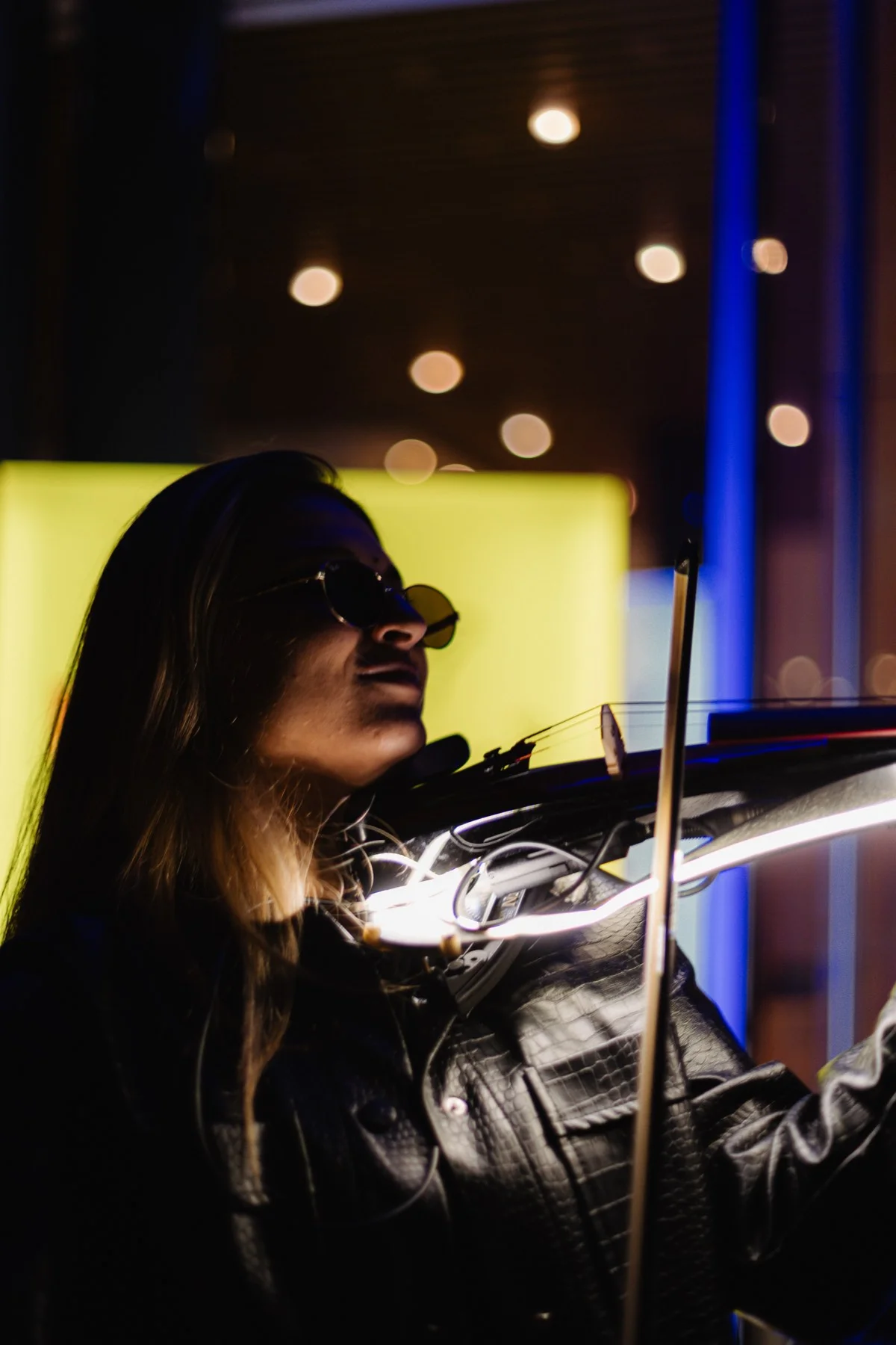 Eine Musikerin mit Sonnenbrille und schwarzer Lederjacke spielt am Abend eine leuchtende elektrische Geige.