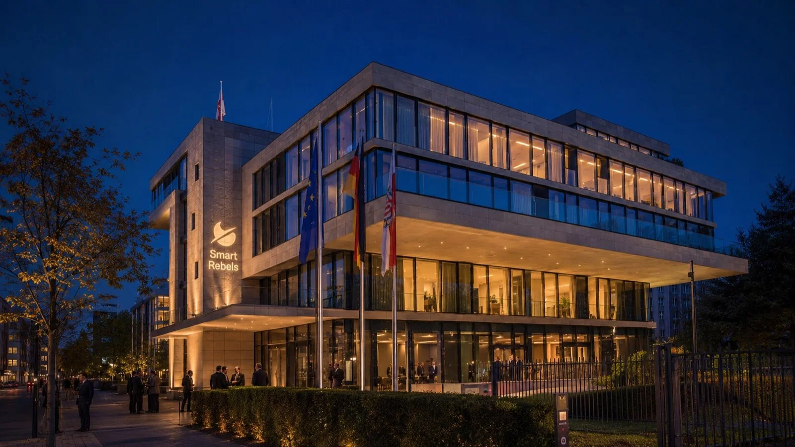 Hessische Landesvertretung Berlin in der blauen Stunde, beleuchtete Fassade mit Smart-Rebels-Projektion, davor Europa-, Deutschland- und Hessenflagge