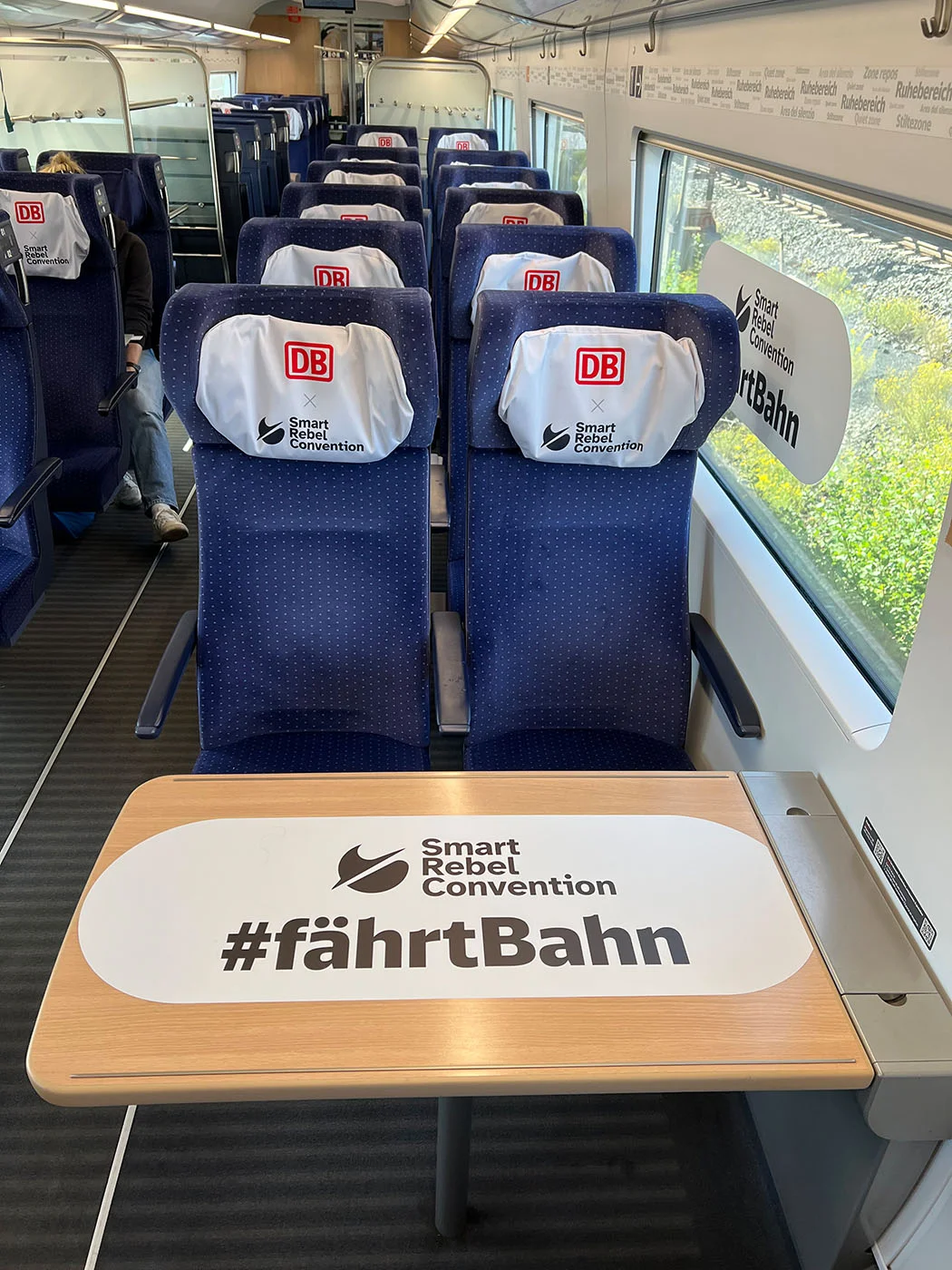 Zugabteil mit Kopfstützenbezügen „DB × Smart Rebel Convention“ und Tischaufkleber „#fährtBahn“